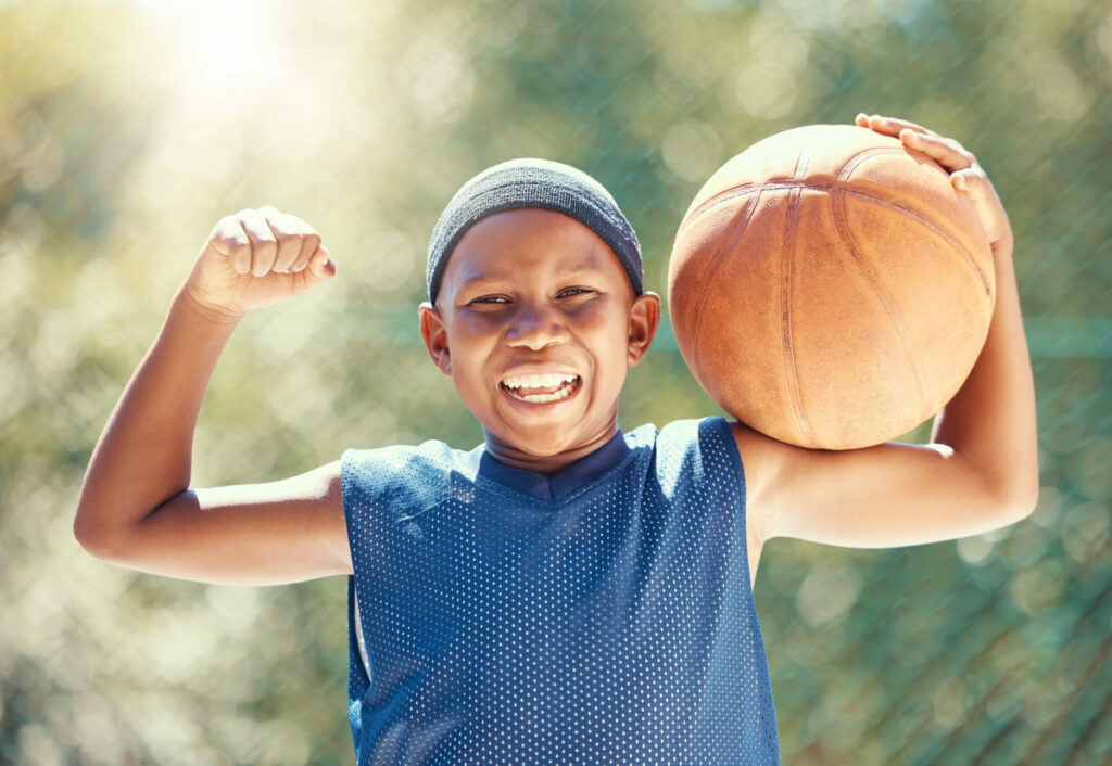 Kleiner Junge beim Anspannen des Bizeps und halten eines Basketballs.