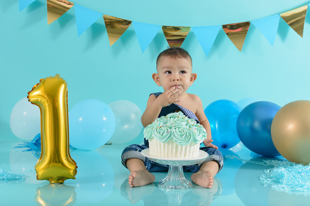 Der erste Geburtag - 1 jähriges Kind mit Geburtstagskuchen und Ballons im Hintergrund.