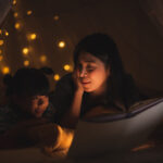 Einschlafhilfe für Kinder - Mutter liest ihrer Tochter eine Gutenachtgeschichte auf dem Bett vor