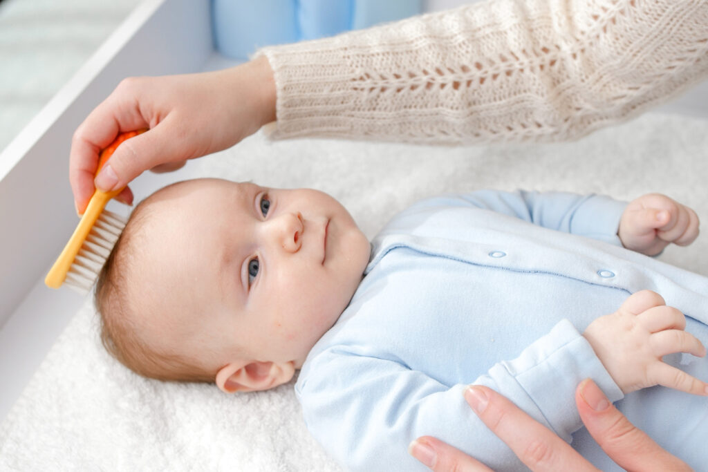 Baby Haare schneiden - Nahaufnahme eines Babys, dass die Haare von seiner Mutter gekämmt bekommt, als Vorbereitung für seinen ersten Haarschnitt als Baby.