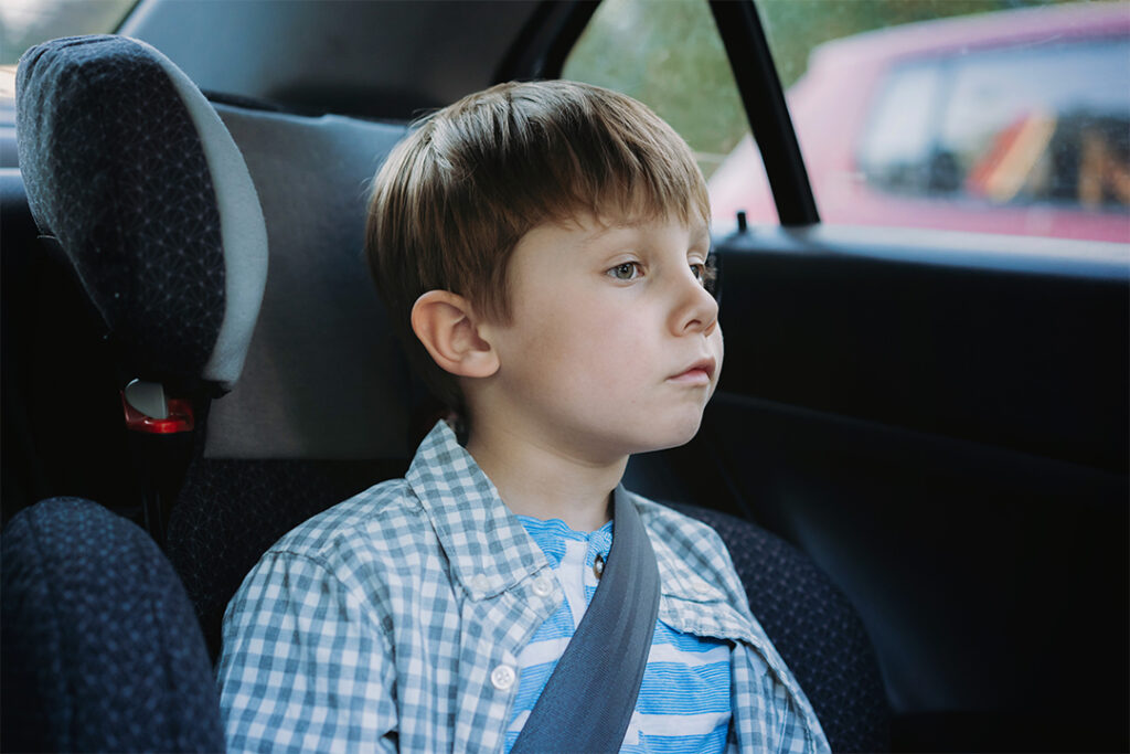 Reiseübelkeit Kinder - Ein Junge mit Reiseübelkeit schaut aus dem Autofenster, um sich abzulenken, weil ihm unwohl ist.