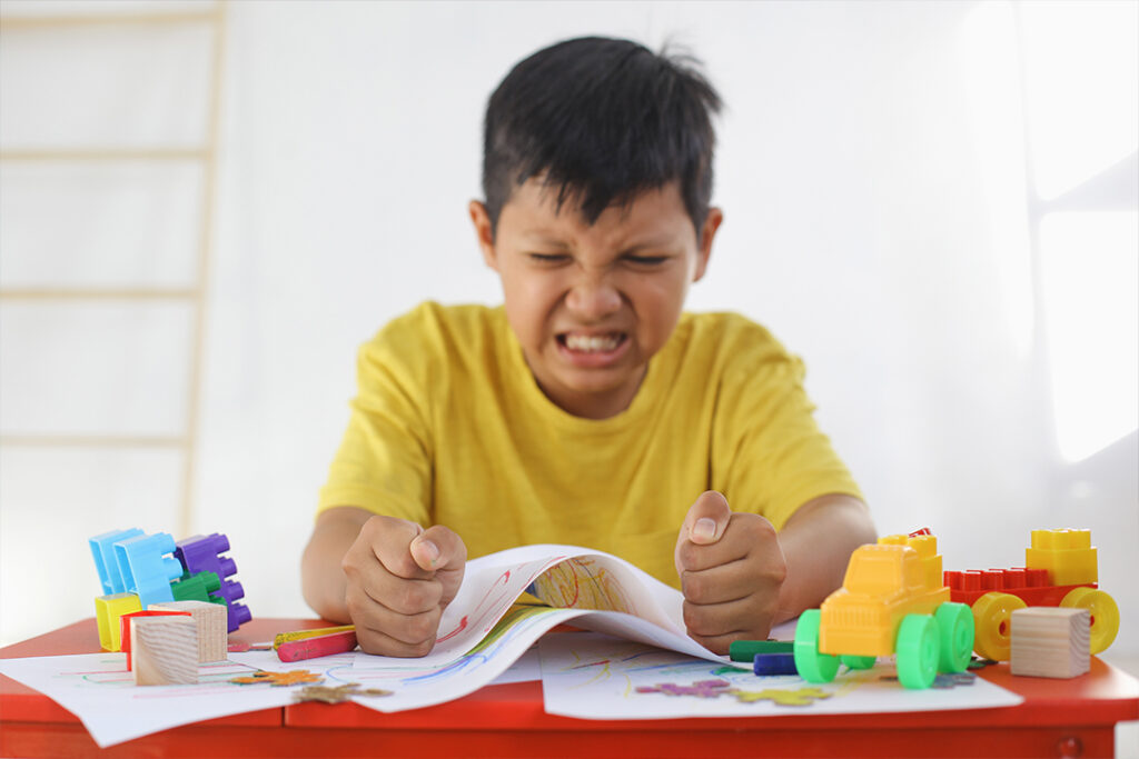 Extreme Wutanfälle bei Schulkindern: Wann sind Wutanfälle bei Kindern nicht mehr normal? Nahaufnahme von einem wütenden Jungen am Kindertisch. Er zerknüllt vor Wut seine Zeichnungen.