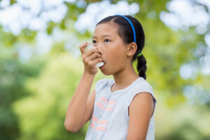 Asthma bei Kindern durch Heuschnupfen. Nahaufnahme eines kleinen Mädchens, das im Freien einen Asthma-Inhalator verwendet, weil ihr die Pollenallergie zu schaffen macht.
