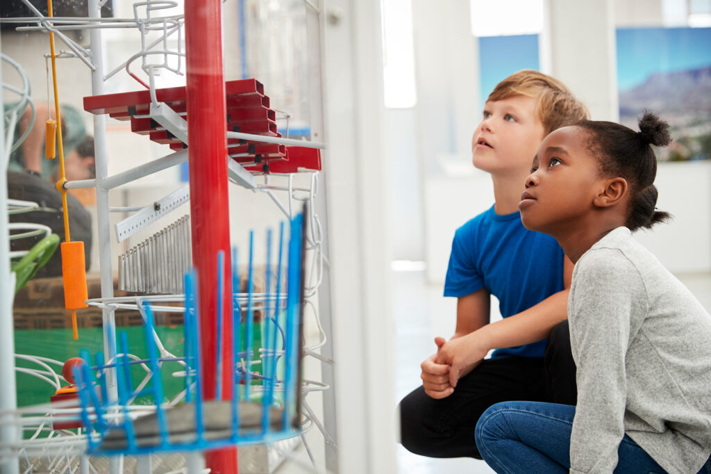 Ein Junge und ein Mädchen im Schulalter, entdecken eine Klang Murmelbahn in einem interaktiven Museum und schauen zu, wie die Murmel sich ihren Weg bahnt.