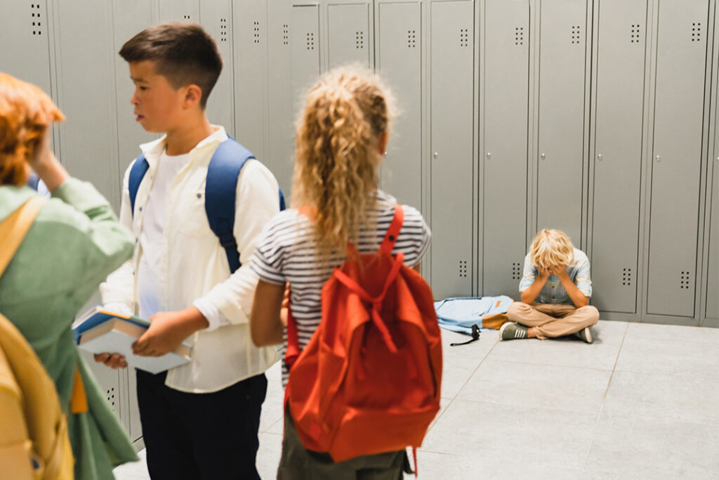 Ein einsames Kind wird ausgeschlossen, das auf dem Boden der Schulhalle weint. Seine Klassenkameraden ignorieren ihn dabei.